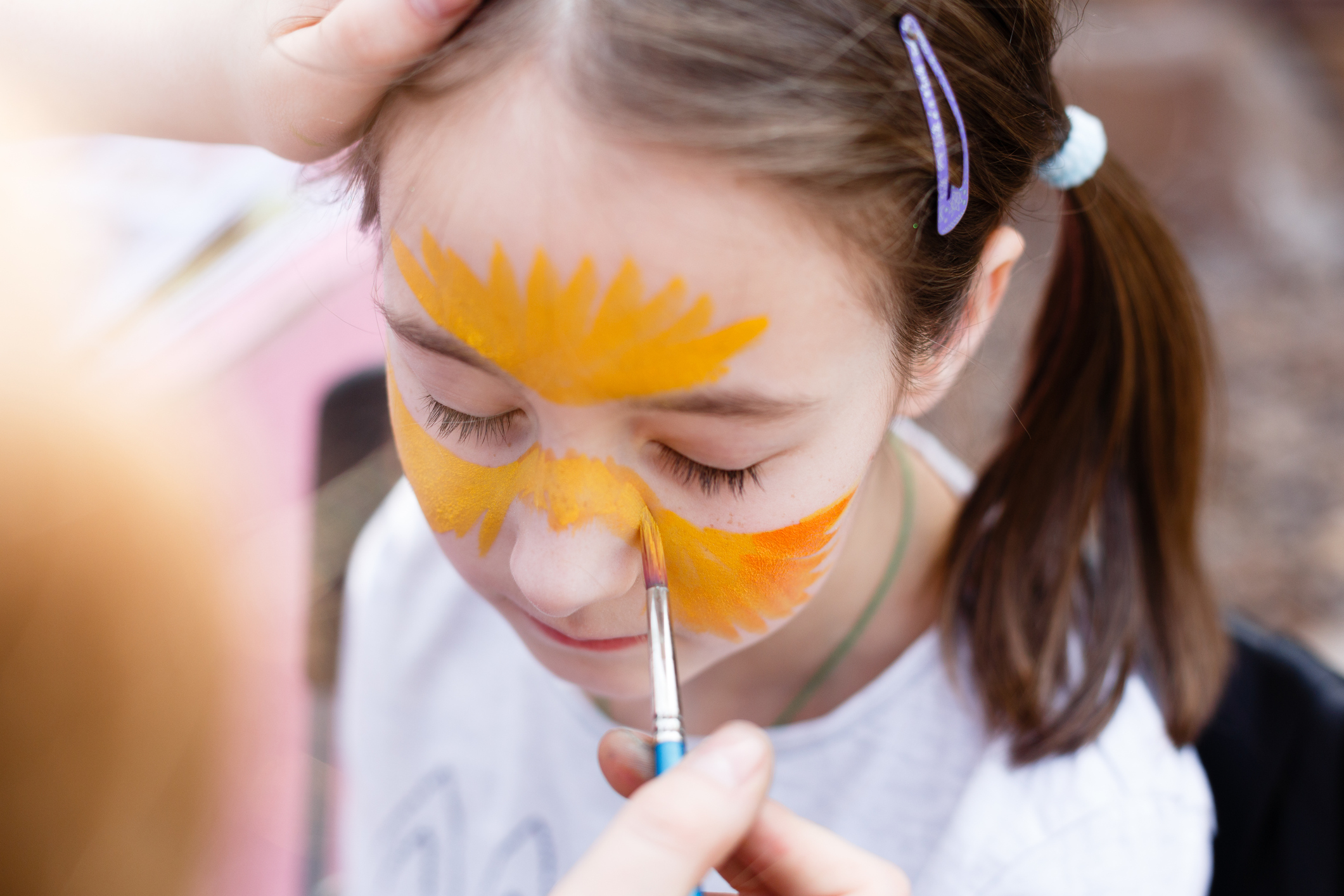 Child animator, artist's hand draws face painting to little girl. Child with funny face painting. Painter makes tiger eyes at girl's face. Children holiday, event, bithday party, entertainment.