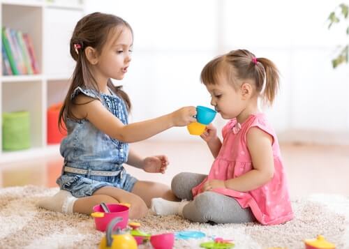 Duas meninas brincando de tomar chá com brinquedos coloridos